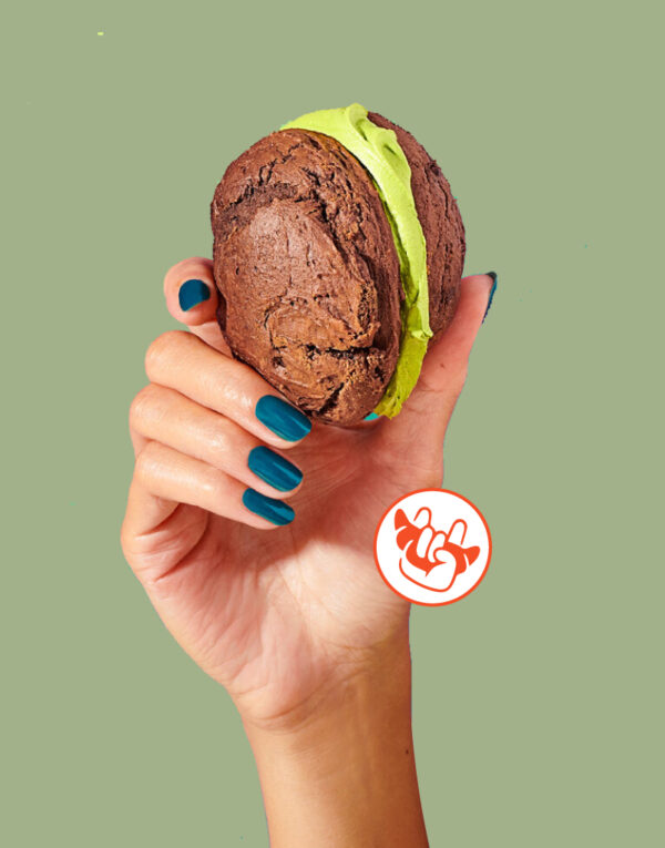 En esta imagen sale una mano que sujeta un macaron con té matcha en el interior. Tiene un fondo verde